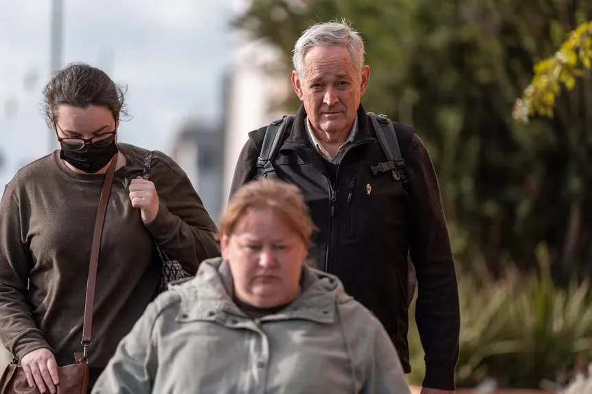 Ian Wilkinson caminha ao lado de duas mulheres.' typeof='foaf:Image' title=